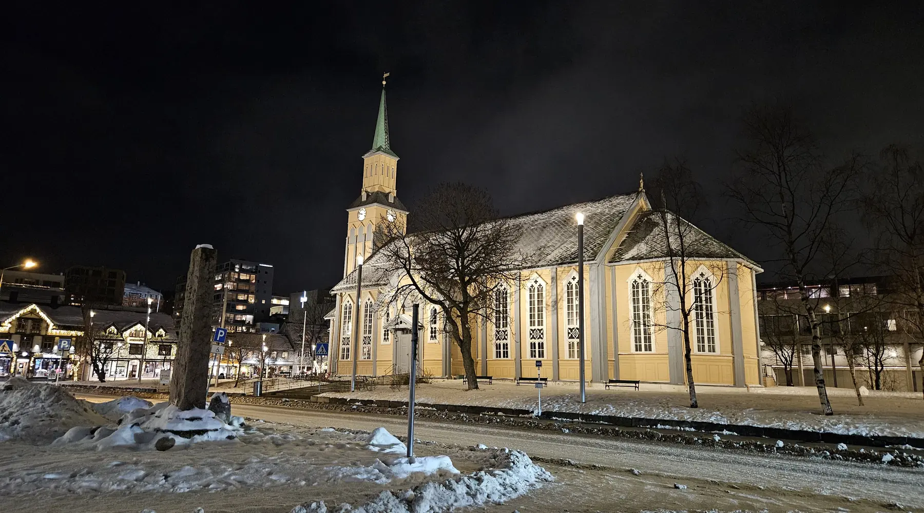 Tromsø Cathedral at night, a lit yellow church in a snowy square under a dark sky