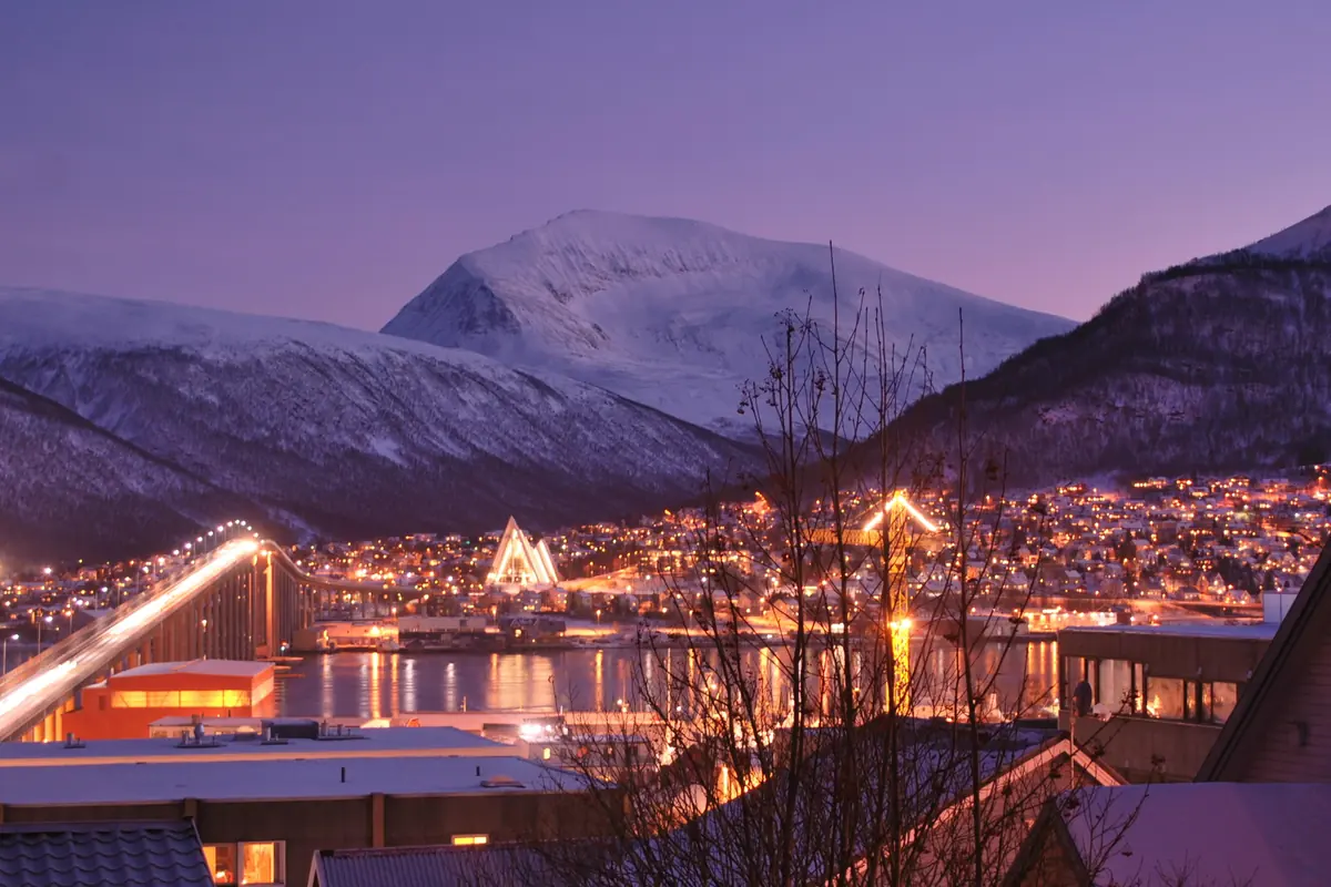 Tromsø in the polar night at twilight, with lit streets, the bridge and snow-covered mountains under a purple sky