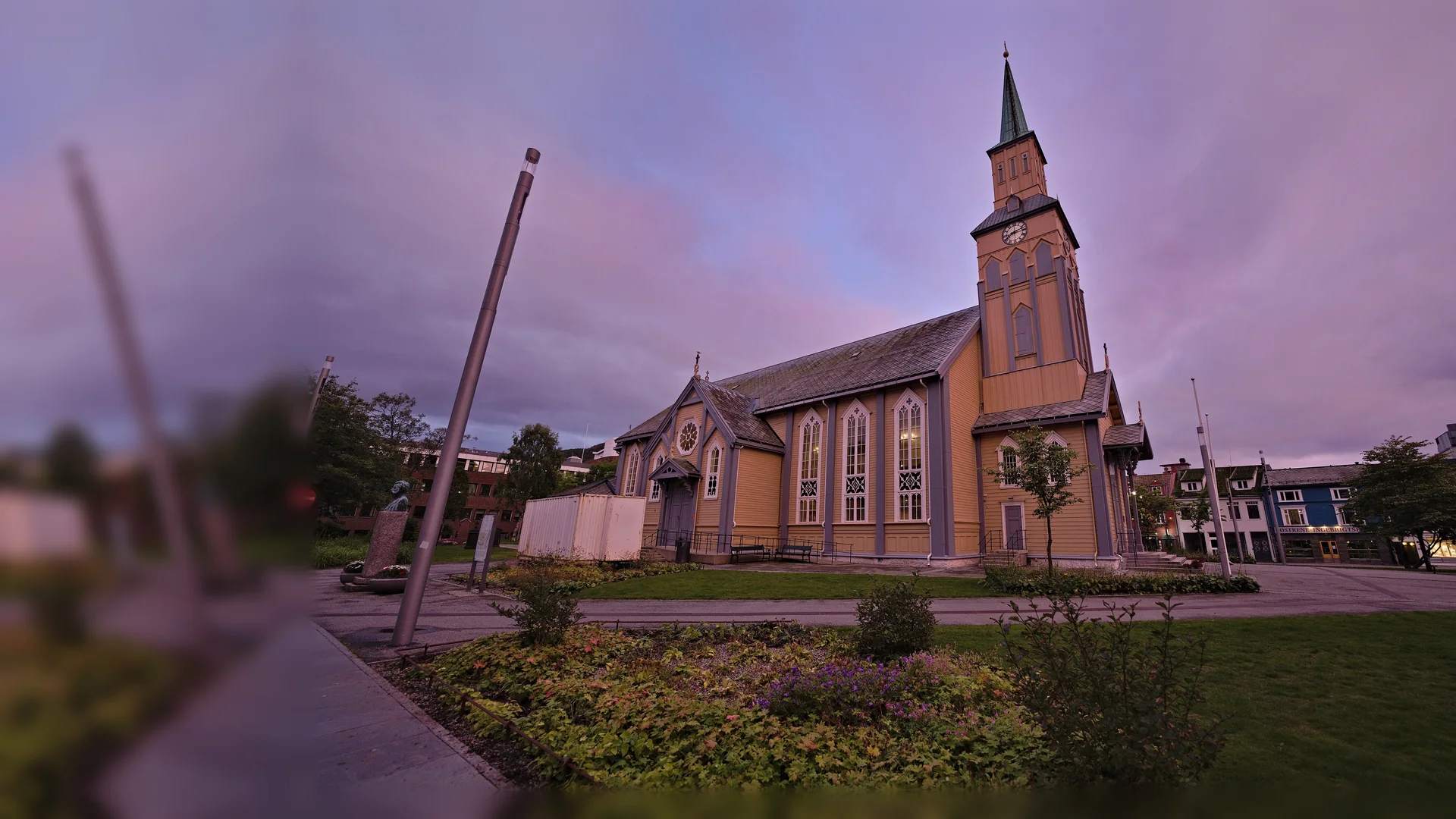 Tromsø Cathedral, a yellow wooden church with a tall green-capped tower, standing in its park under a pink and violet dusk sky